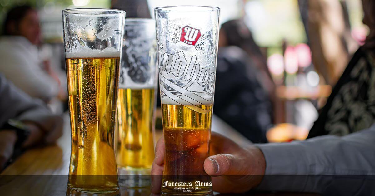 windhoek draught feature image - Person holding a beer with a few other beers and people in the background