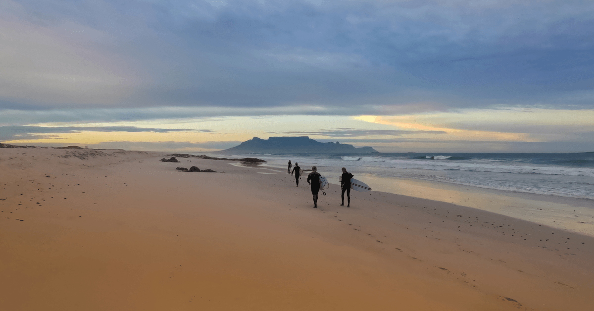 Surfers walking down Bloubergstrand to go surf with Table Mountain in the back drop 