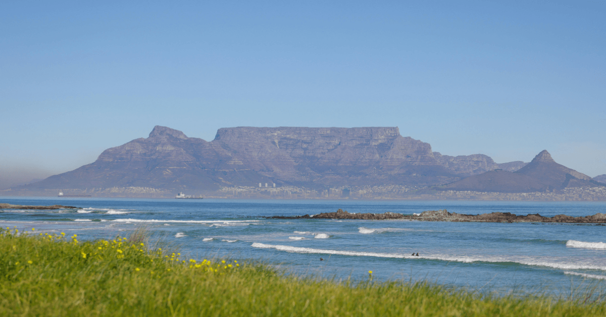 View from Melkbosstrand of surfers in the water and Table Mountain 