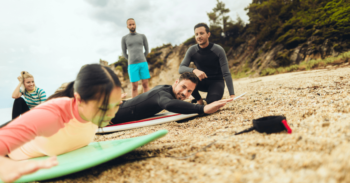 Surf Lessons Cape Town - Beginner surfers being taught how to paddle on the beach by there surf instructors 