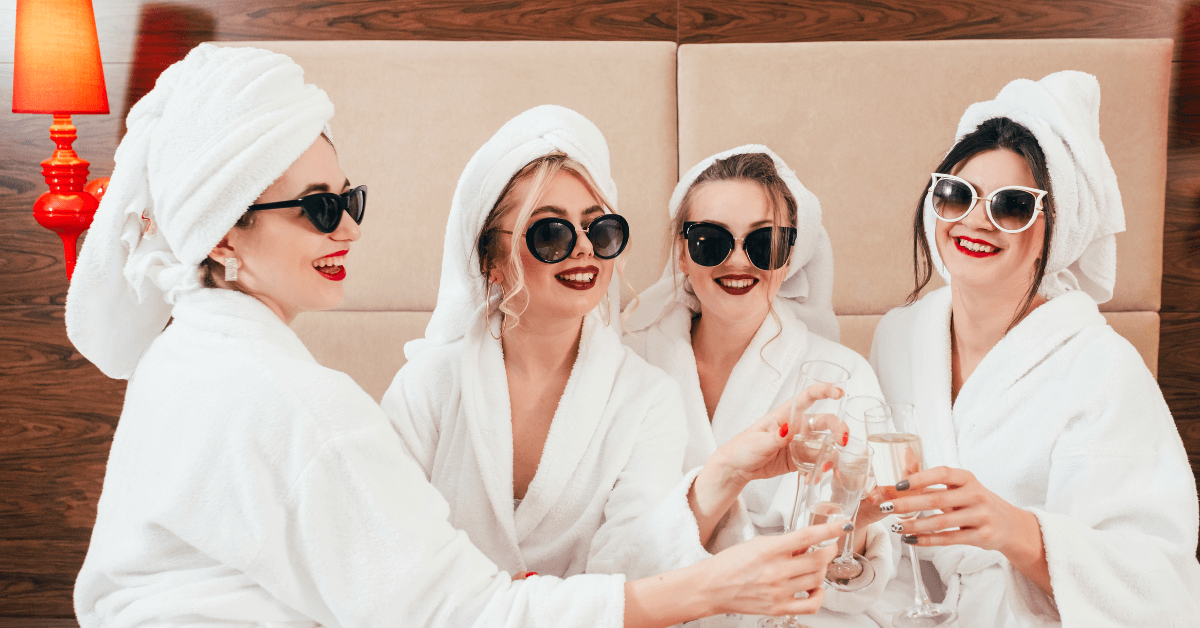 Woman dressed in spa gowns drinking a glass of champagne in celebration of a bachelorette party 